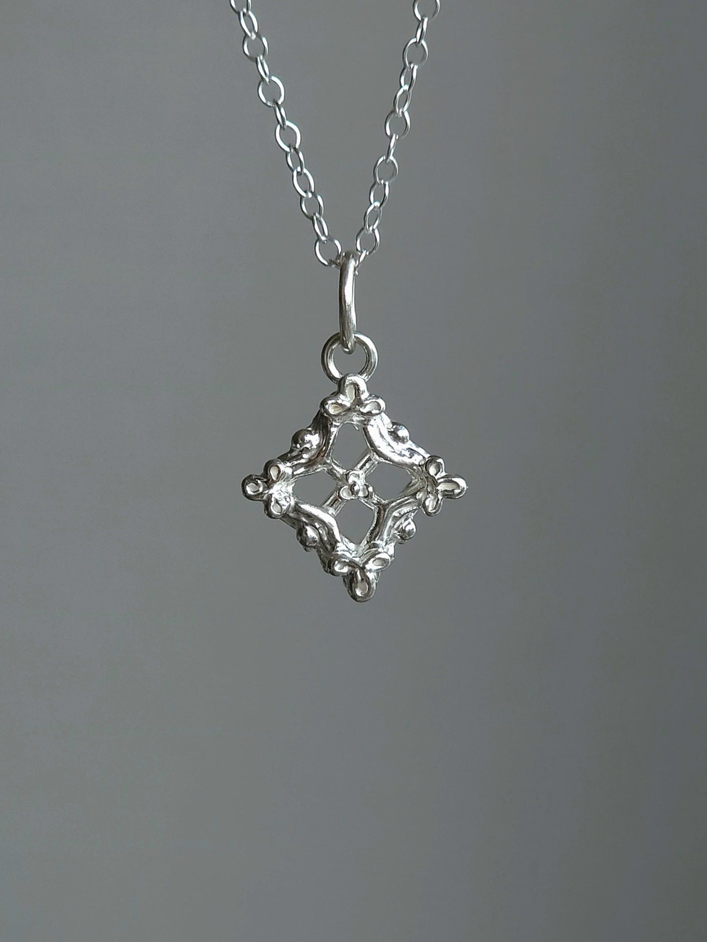 A silver pendant necklace featuring a decorative openwork diamond-shaped charm with a small bird motif, suspended from a delicate silver chain against a neutral gray background.