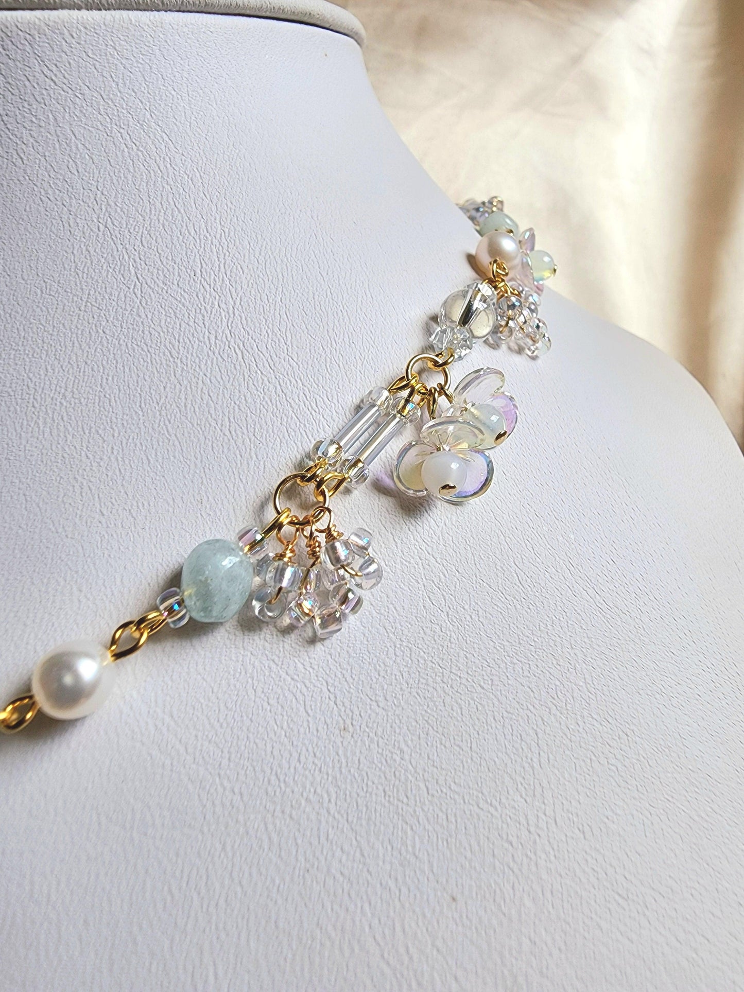 This handcrafted choker is composed of opalite, baby blue bugle beads, freshwater pearls, acrylic flower beads, seed beads, and gold-plated findings for an ethereal, soft, and detailed finish.