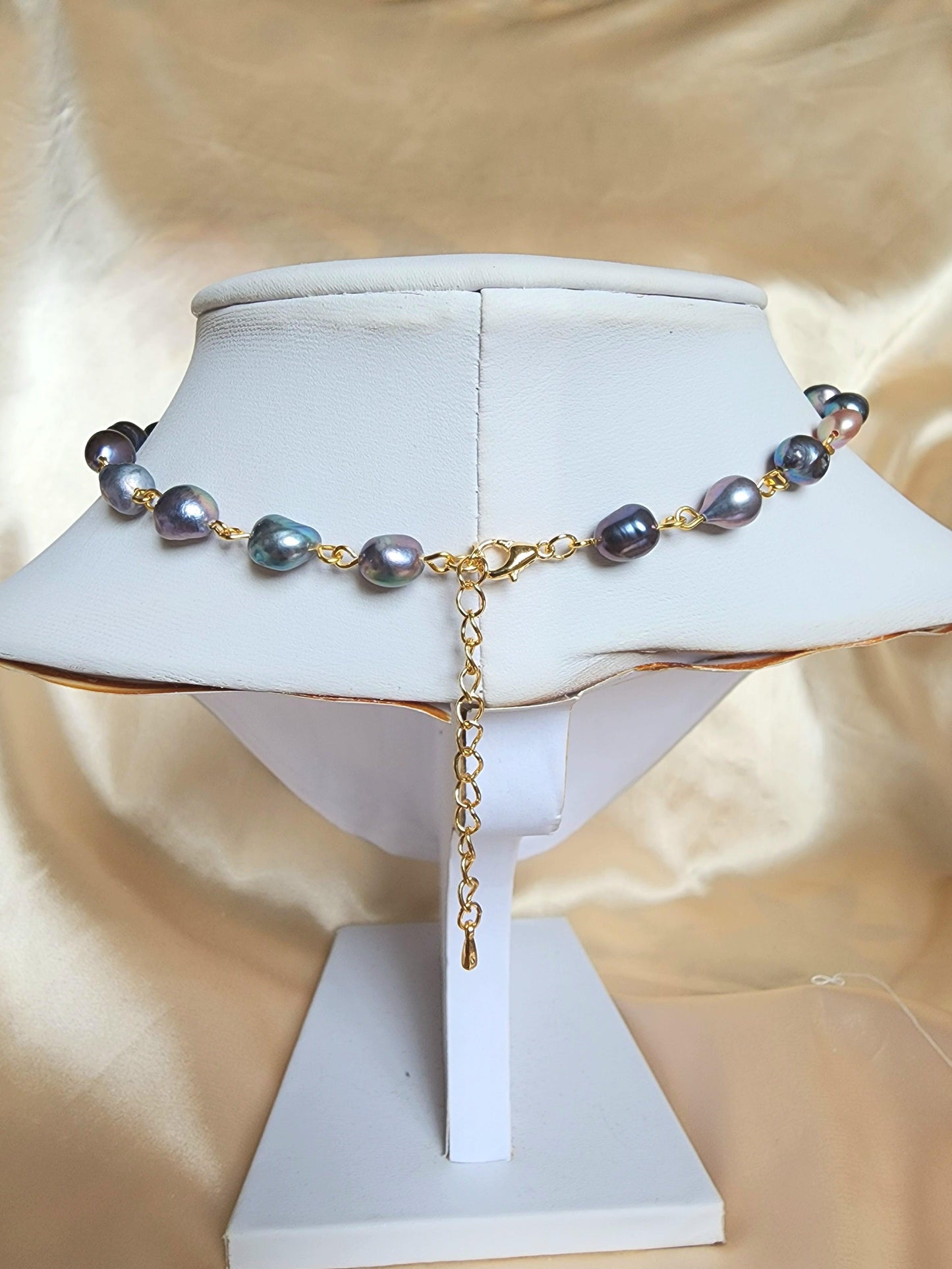 This elegant choker is crafted with gold-plated brass, stainless steel findings, and tarnish-resistant copper wire, featuring a romantic design of flower-shaped black freshwater pearls alongside iridescent black seed bead details.