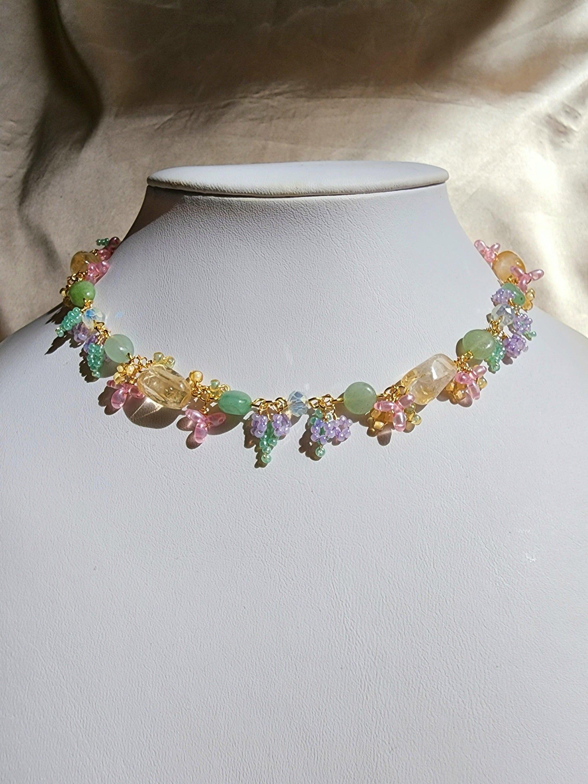 A vibrant pastel necklace with flower and leaf details made of seed beads. Green aventurine and citrine gives the impression of a warm afternoon in the forest with enchanting seed bead flowers and plants in pastel pink, purple, yellow, and green. A dreamy piece fit for forest fairies.