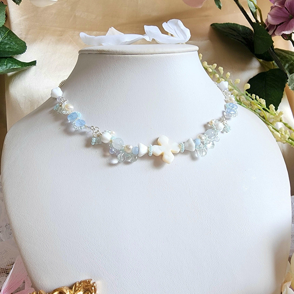 
                  
                    The Knights of the Sky are an esteemed class that traverse the skies, their silhouettes framed by the backdrop of white-tinted, petal-laden clouds. This handcrafted necklace is constructed with a shell centerpiece, vintage glass beads, Czech glass beads, freshwater pearls, and silver-plated accents.
                  
                
