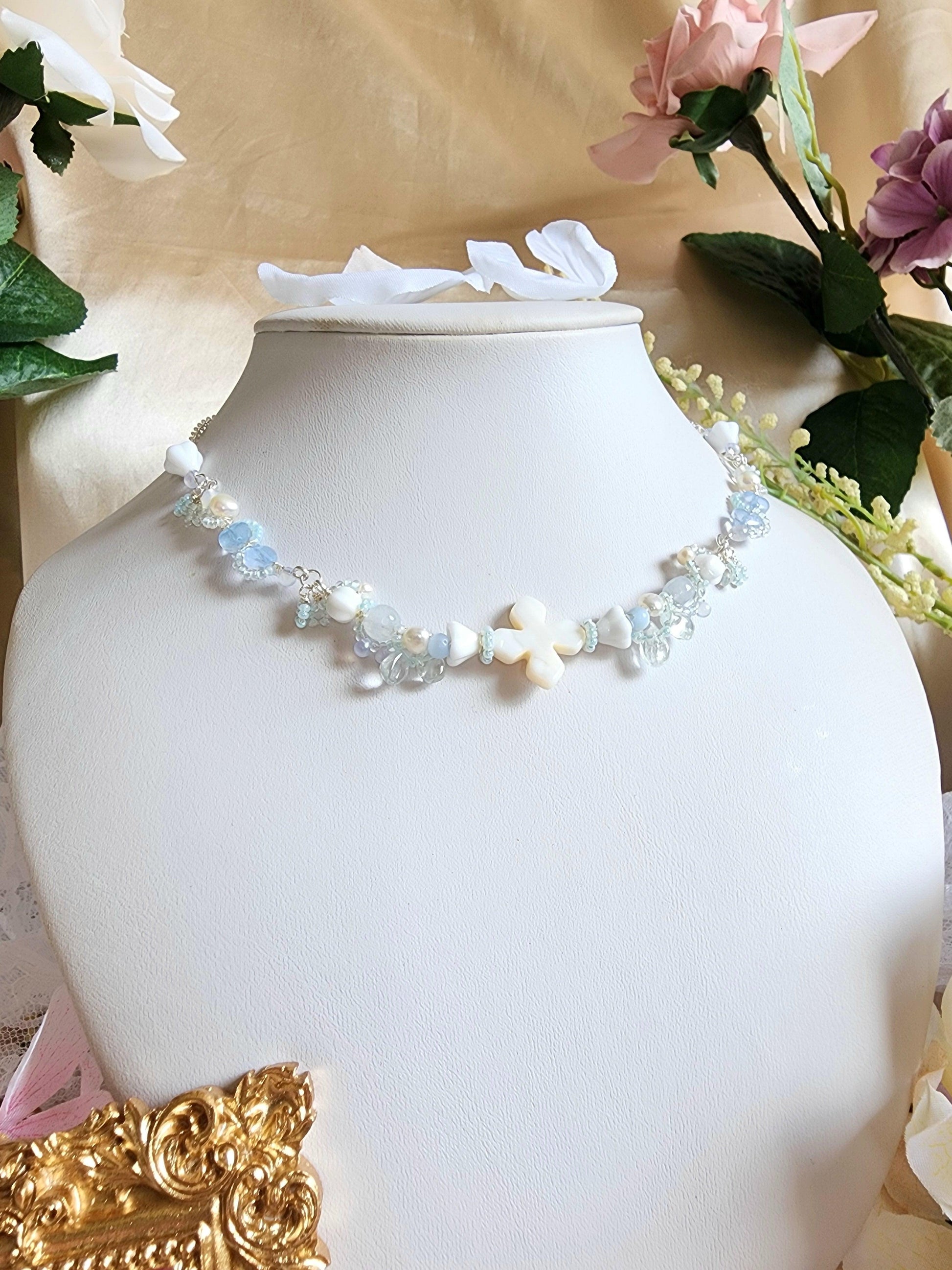 The Knights of the Sky are an esteemed class that traverse the skies, their silhouettes framed by the backdrop of white-tinted, petal-laden clouds. This handcrafted necklace is constructed with a shell centerpiece, vintage glass beads, Czech glass beads, freshwater pearls, and silver-plated accents.