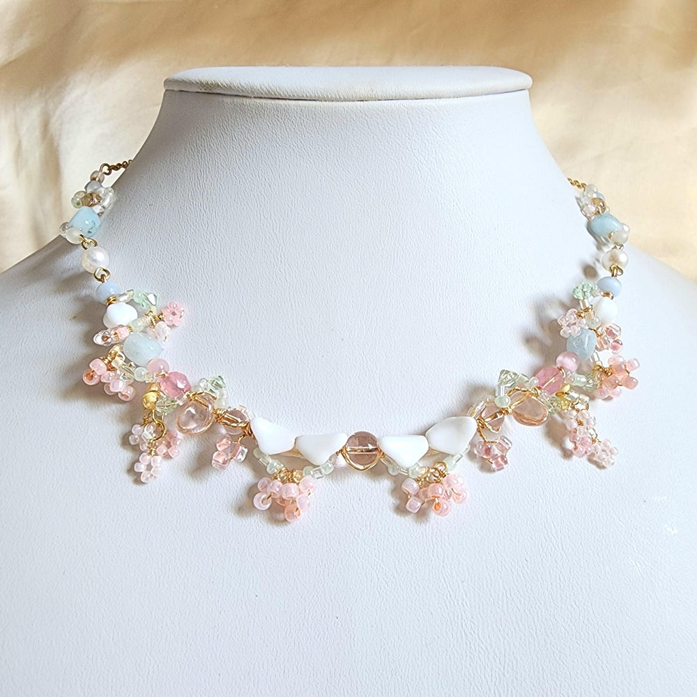 
                  
                    The vista of the Pink Mountain mesmerizes all who witness it, its regal form proudly standing amidst a pale azure sky. Visitors are drawn in by the cascading vines adorned in delicate pink blossoms, lending their hues to the iconic mountain. Artfully crafted with vintage glass beads, Czech glass beads, aquamarine, freshwater pearls, brass artistic wire, and gold-plated findings, Mirage of the Pink Mountain is a unique handcrafted necklace.
                  
                