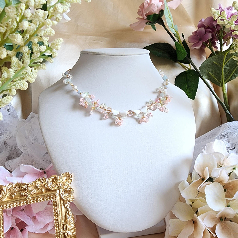 
                  
                    The vista of the Pink Mountain mesmerizes all who witness it, its regal form proudly standing amidst a pale azure sky. Visitors are drawn in by the cascading vines adorned in delicate pink blossoms, lending their hues to the iconic mountain. Artfully crafted with vintage glass beads, Czech glass beads, aquamarine, freshwater pearls, brass artistic wire, and gold-plated findings, Mirage of the Pink Mountain is a unique handcrafted necklace.
                  
                